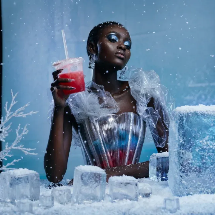 AI-generated portrait of a woman in a sparkling silver bustier sipping a red slushie at an ice-block bar surrounded by snowflakes and frosted branches.