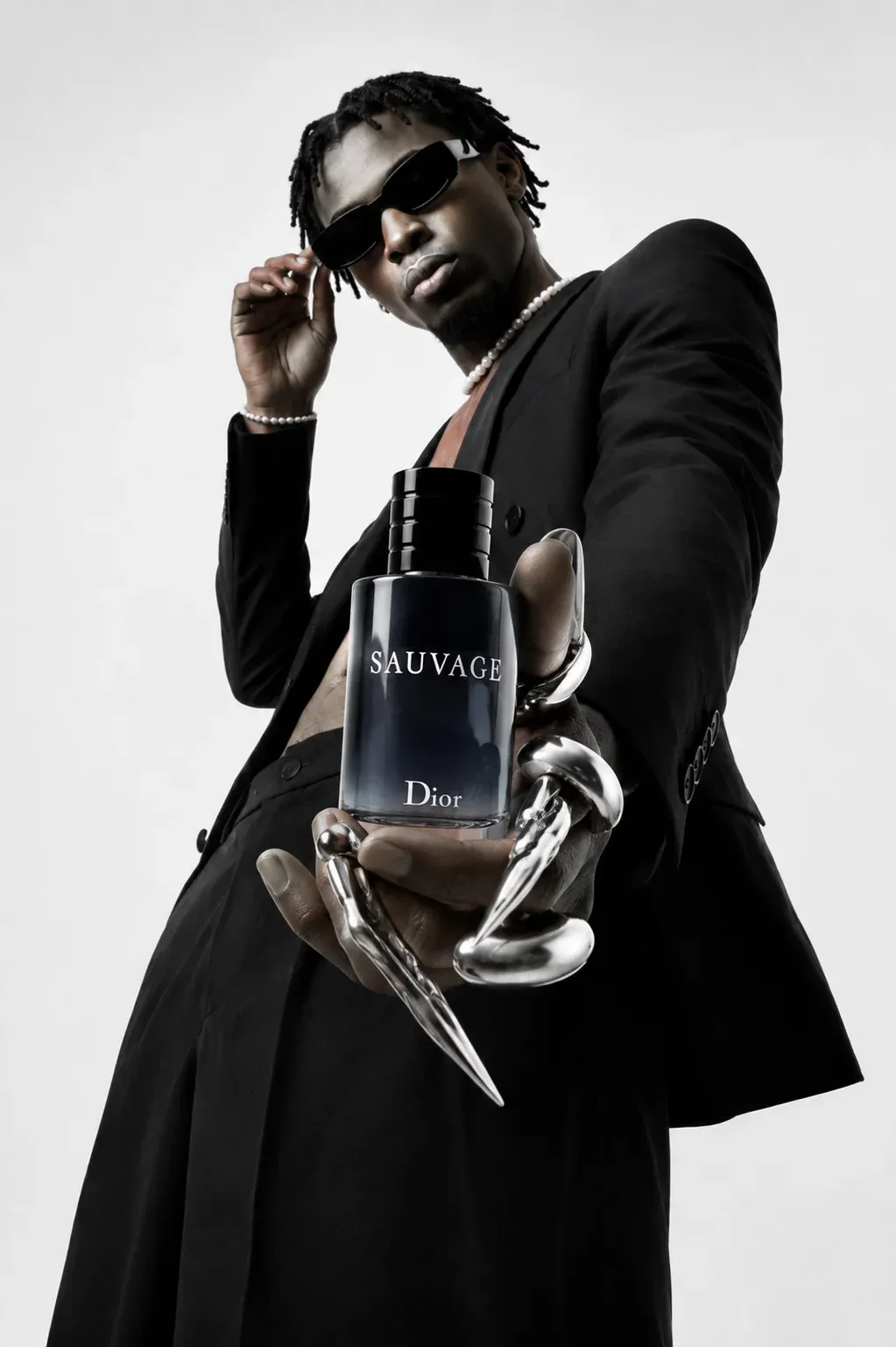 Editorial Dior Sauvage fragrance ad featuring a Black male model in a black suit and sunglasses holding a Sauvage bottle with liquid silver claws wrapped around his fingers