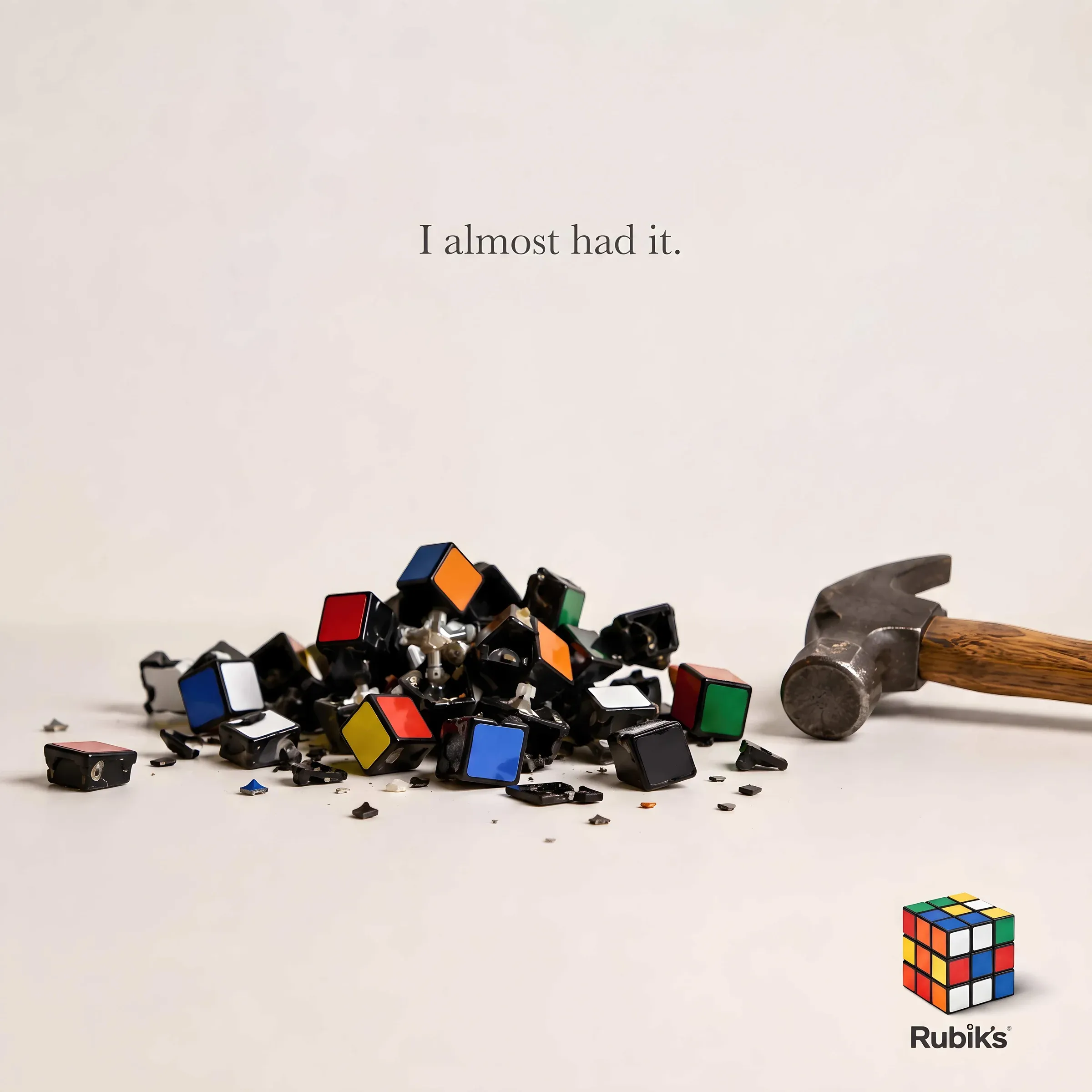 Minimalist Rubik is Cube ad showing a smashed cube of shattered plastic tiles next to a claw hammer on a beige backdrop with the copy line I almost had it.